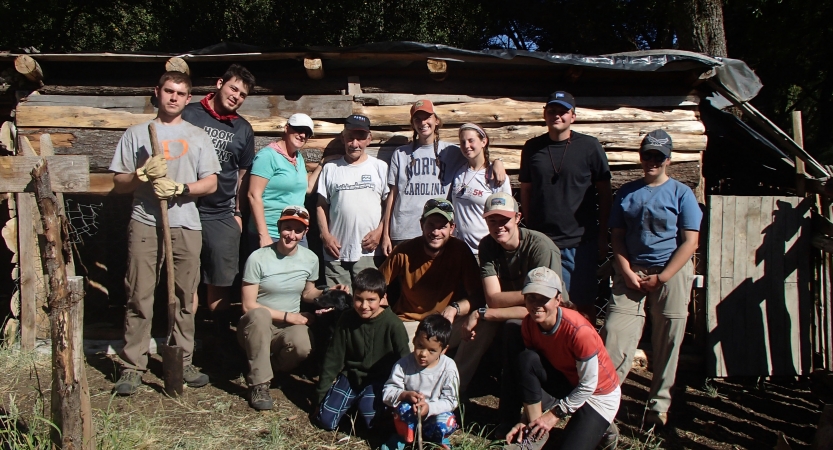 A group of people pose for a photo in front of large pieces of wood. 